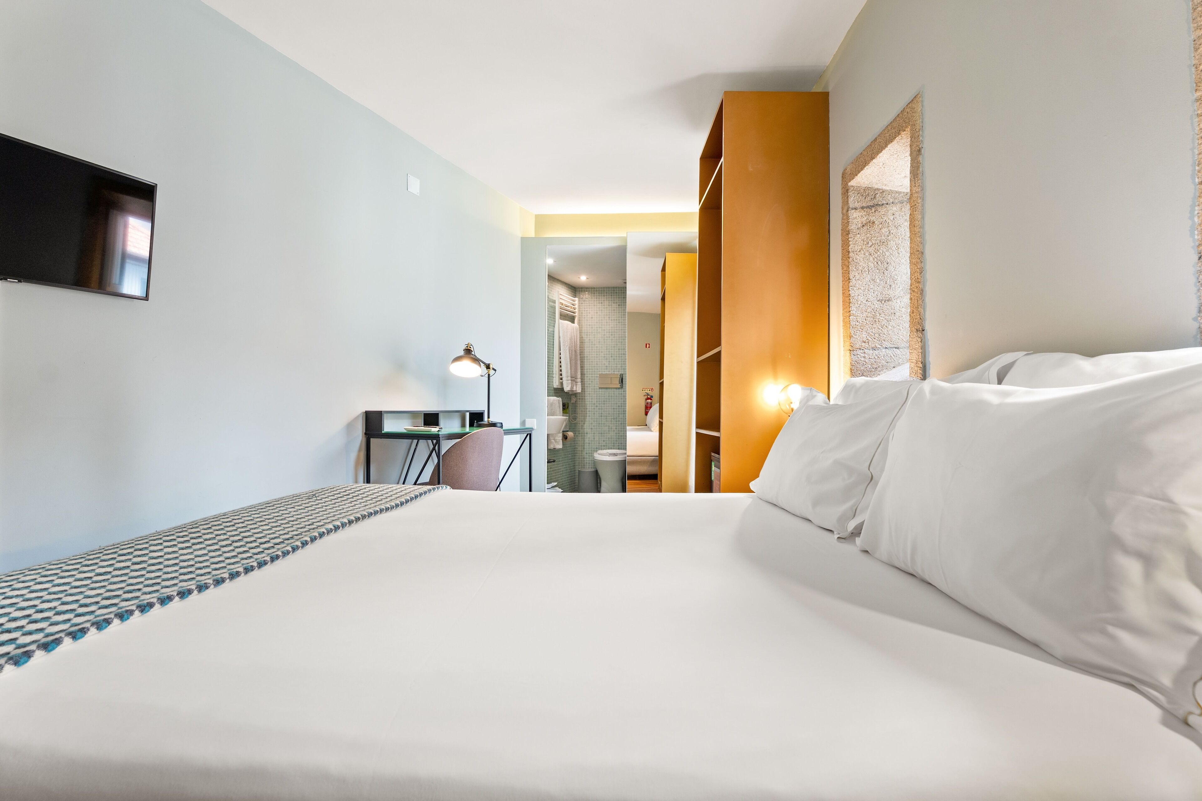 Una habitación de hotel con una cama grande, un escritorio con silla, televisión y baño visible a través de una puerta abierta.