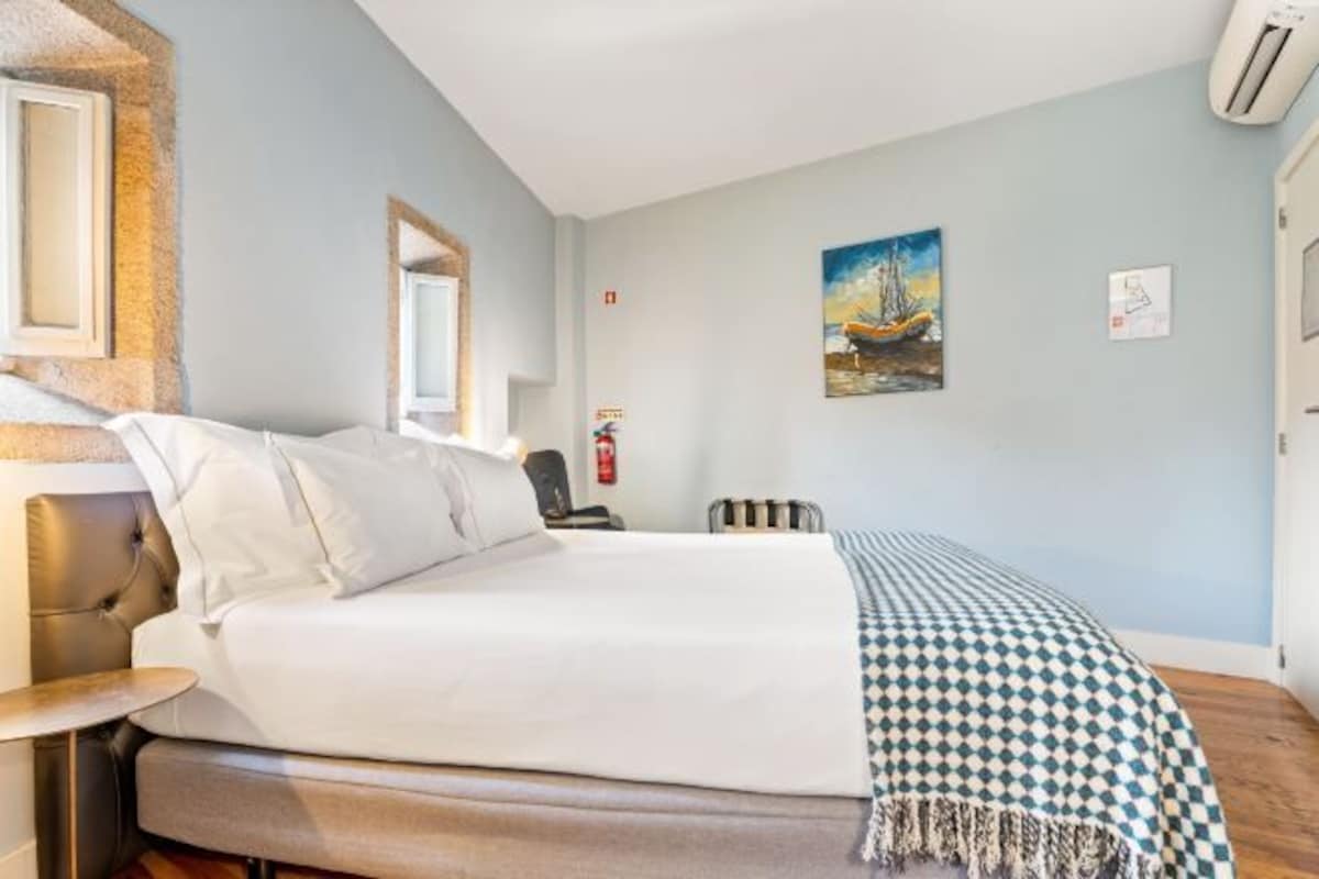A neatly made bed with white linens, a checkered throw blanket, and a wooden headboard.