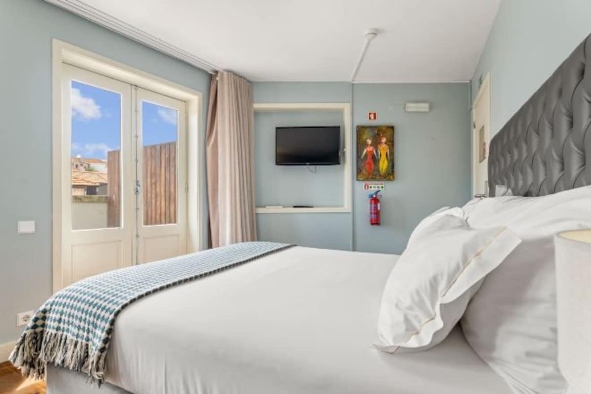 A bedroom with a bed, a television mounted on the wall, and a window with curtains.
