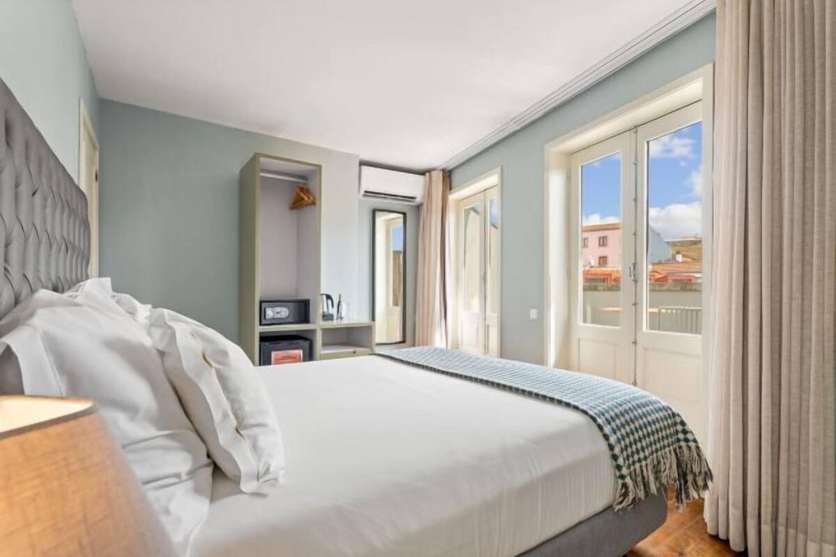 A hotel room with a large bed, a wardrobe, a desk, and a view of the city through the window.