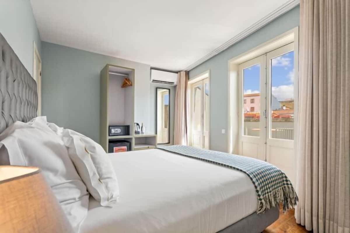 Ein Hotelzimmer mit einem großen Bett, einem Schrank, einem Schreibtisch und Blick auf die Stadt durch das Fenster.