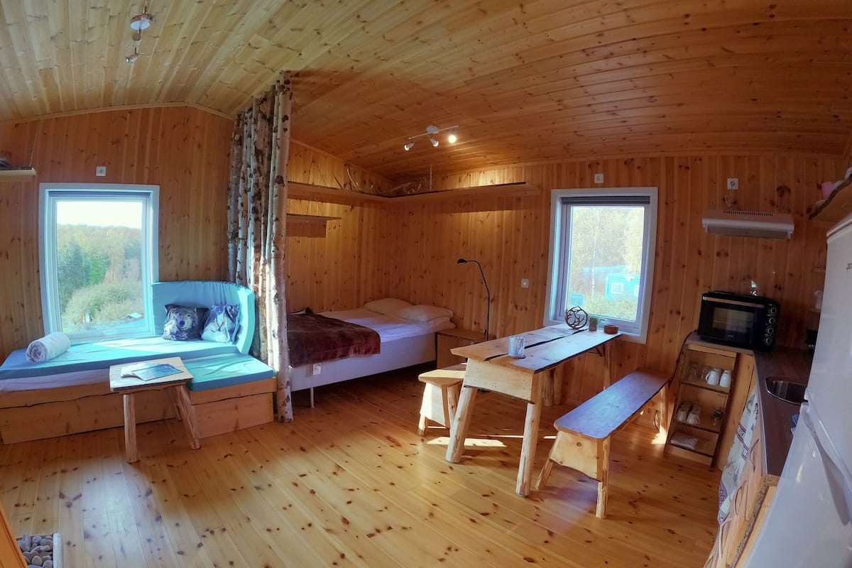 Une cabane dotée d’un coin salon confortable, d’un petit lit, d’une table en bois et d’une kitchenette.
