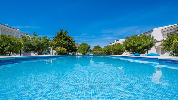 A clear blue swimming pool surrounded by white buildings and green trees. - Apartment near the beach Avus in Alcudia (Alcúdia)