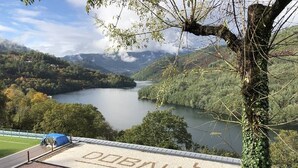 A building with a roof featuring a deer silhouette and the word "DOBALU" on it, overlooking a lake surrounded by hills. - Dobau Village (Vieira do Minho)