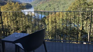 A balcony with a table and chair overlooking a valley with a lake and forested hills. - Dobau Village (Vieira do Minho)