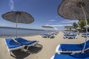 Una playa con filas de sillas azules y sombrillas de mimbre.