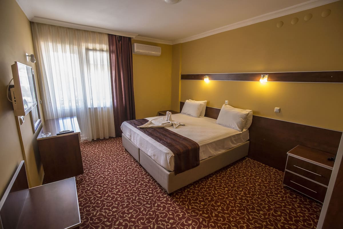 A hotel room with a bed, a desk, a chair, a TV, and a window with curtains.