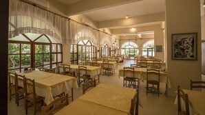Un vaste espace dédié à la salle à manger, avec de nombreuses tables et chaises, de grandes fenêtres dotées de rideaux et un appareil de climatisation fixé au mur.
