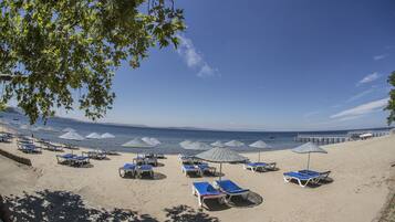 A beach with rows of sun loungers and umbrellas, a pier extending into the water, and a clear blue sky.