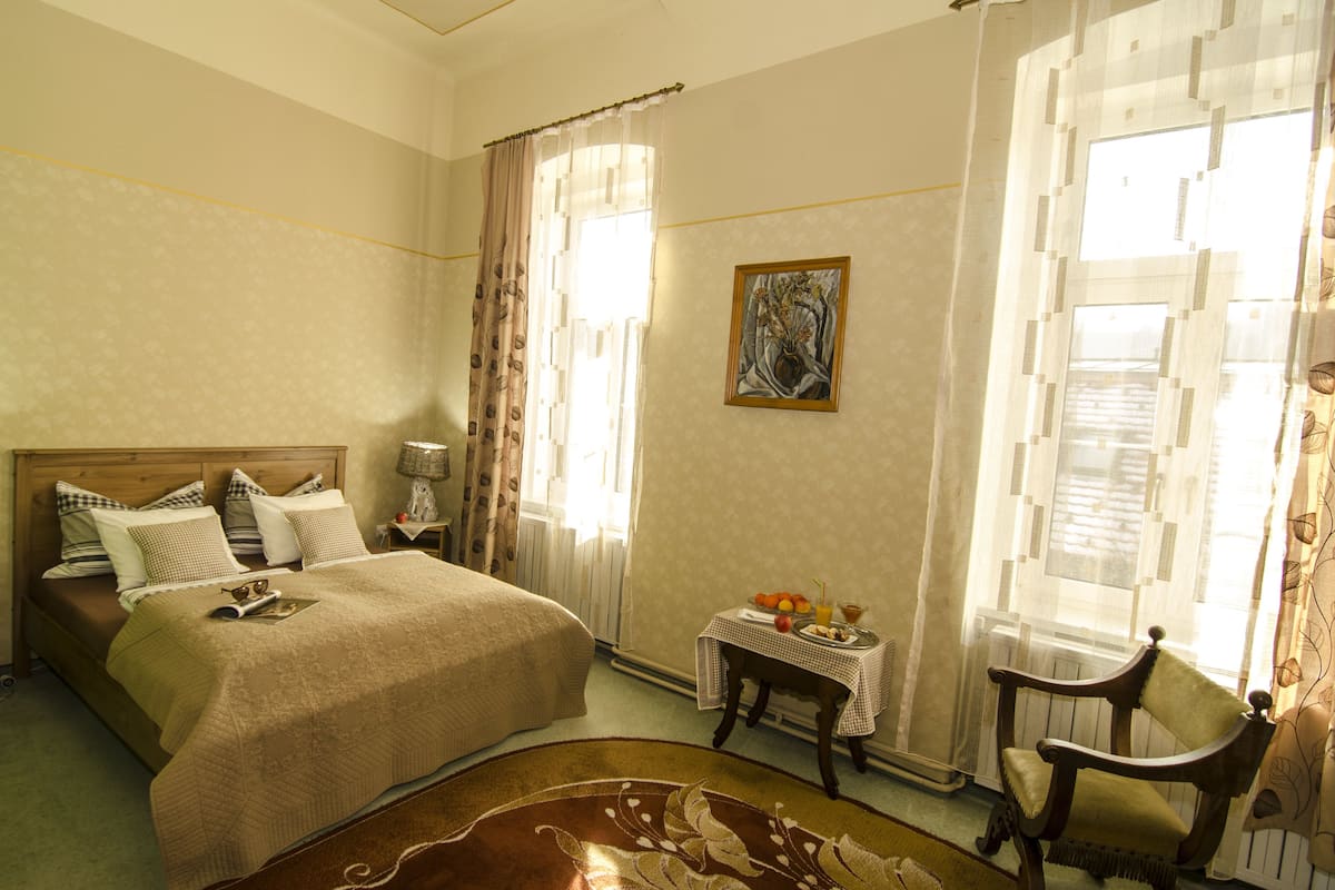 Une chambre à coucher avec un lit, une table de chevet, une chaise, une table avec des fruits et un tableau accroché au mur.