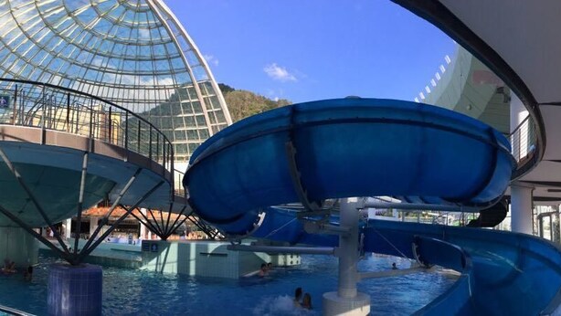 Un parc aquatique intérieur situé à bord d’un navire de croisière, doté d’une grande structure en forme de dôme de verre, de nombreux toboggans et d’une piscine.