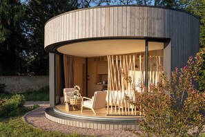 A modern, circular wooden structure with a covered outdoor seating area, including a table and chairs, and a view of the interior. - Clos Marie (Iguerande)