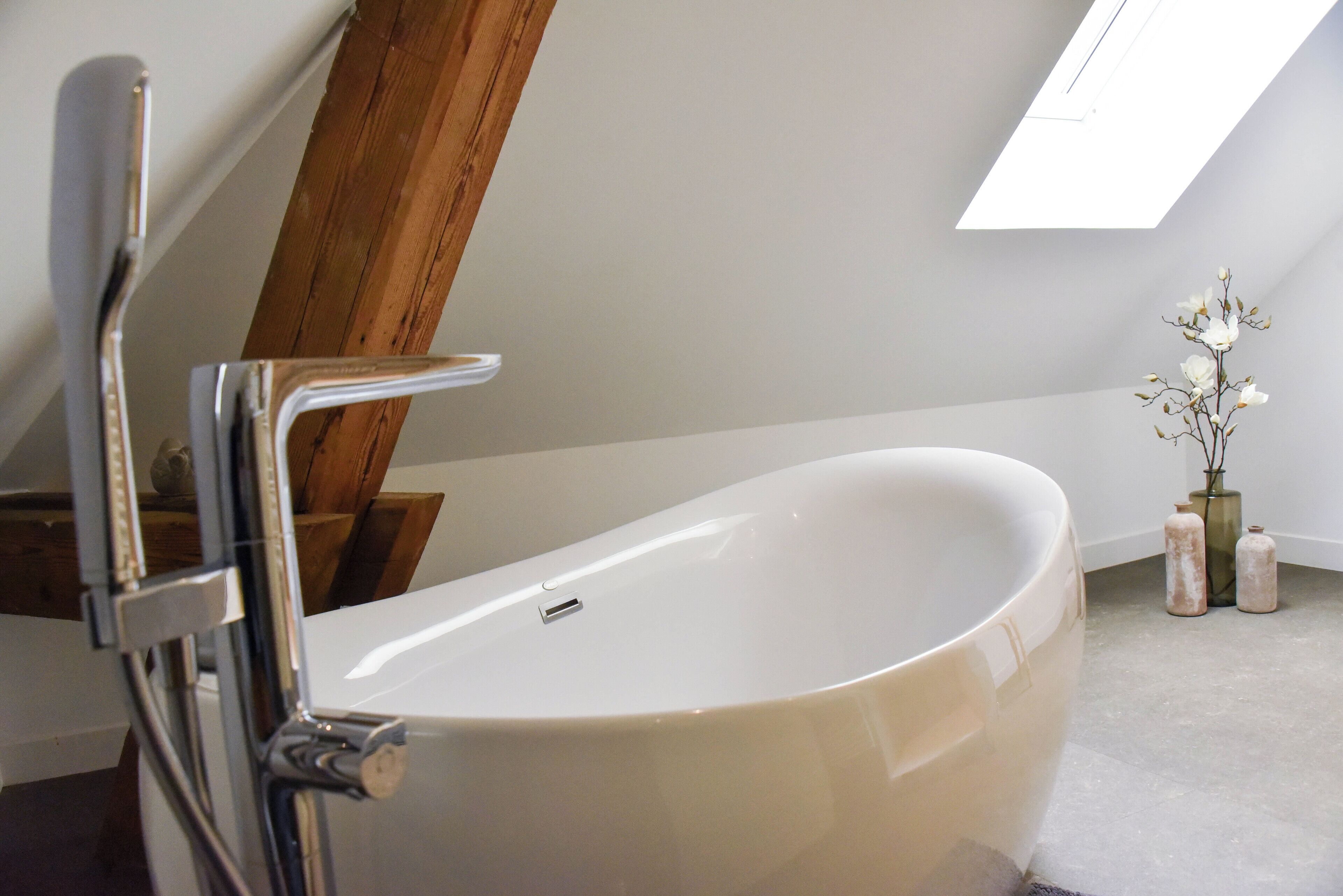 A modern bathroom with a freestanding bathtub, wooden beams, and a skylight.