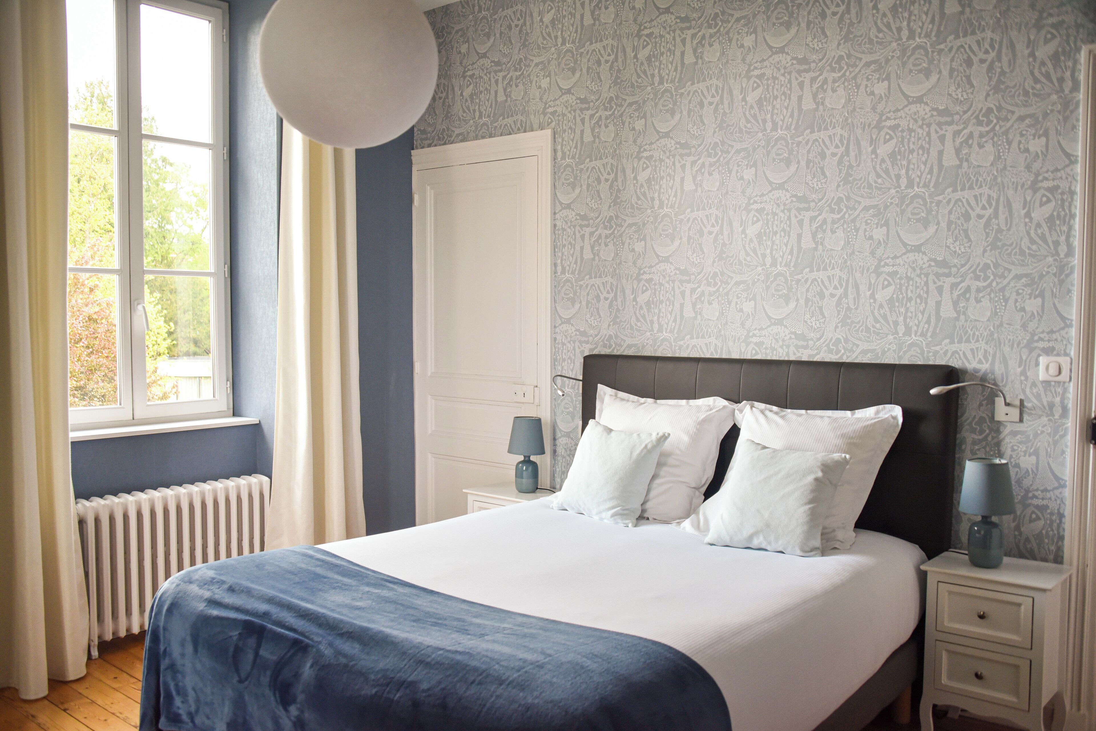 A bedroom with a large bed, a window with curtains, a radiator, and a wall with a patterned design.