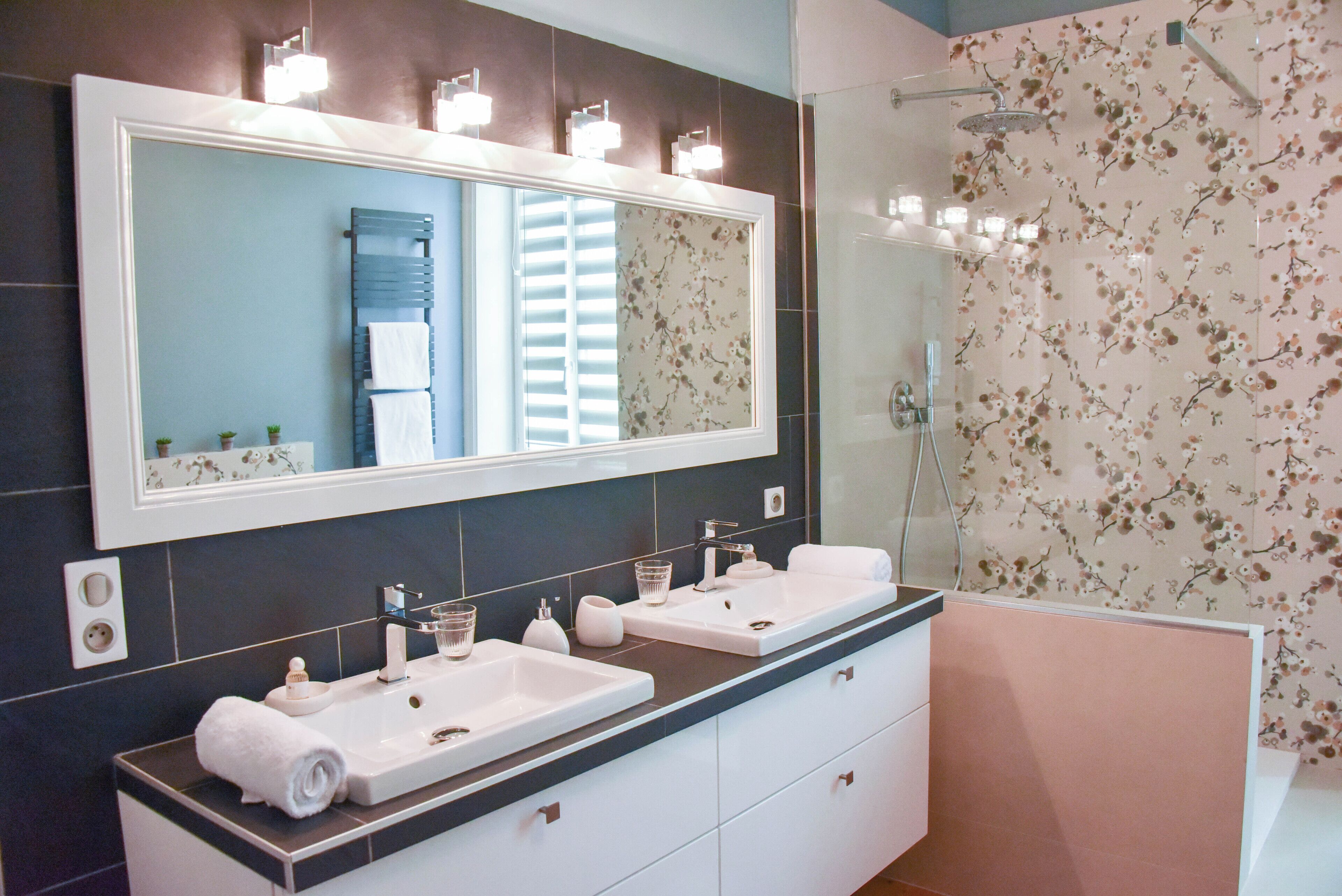 Een moderne badkamer met twee wastafels, een grote spiegel en een douche.