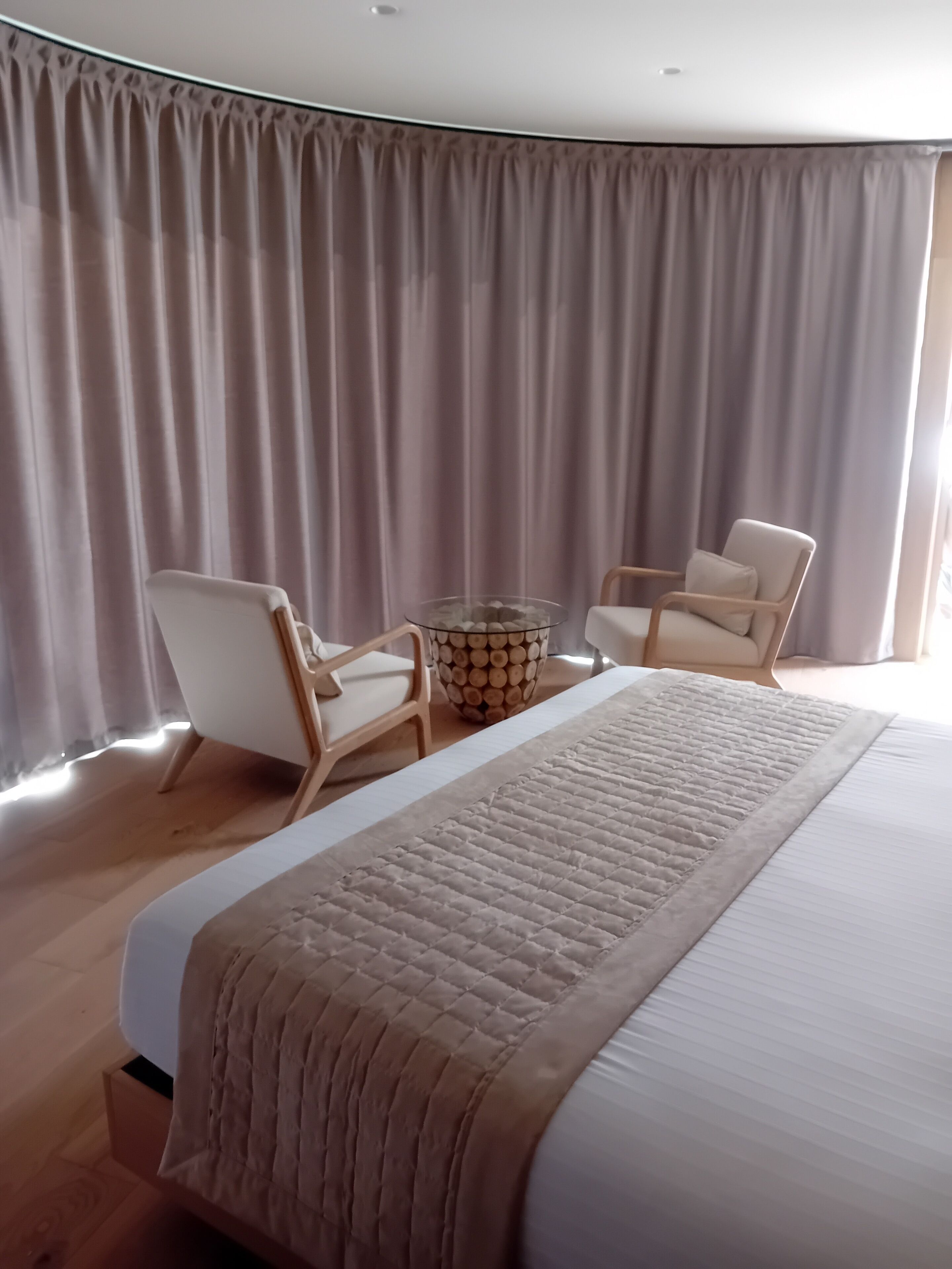 Un dormitorio con una cama grande, dos sillas, una mesita auxiliar y un fondo de cortina.