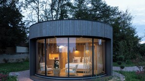 A modern, circular wooden structure with a glass facade, a bed, a seating area, and a small table. - Clos Marie (Iguerande)