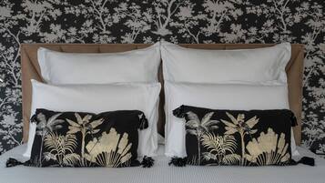 Un letto con lenzuola bianche, due cuscini neri con decorazioni in foglia d'oro e una testiera con motivo floreale.