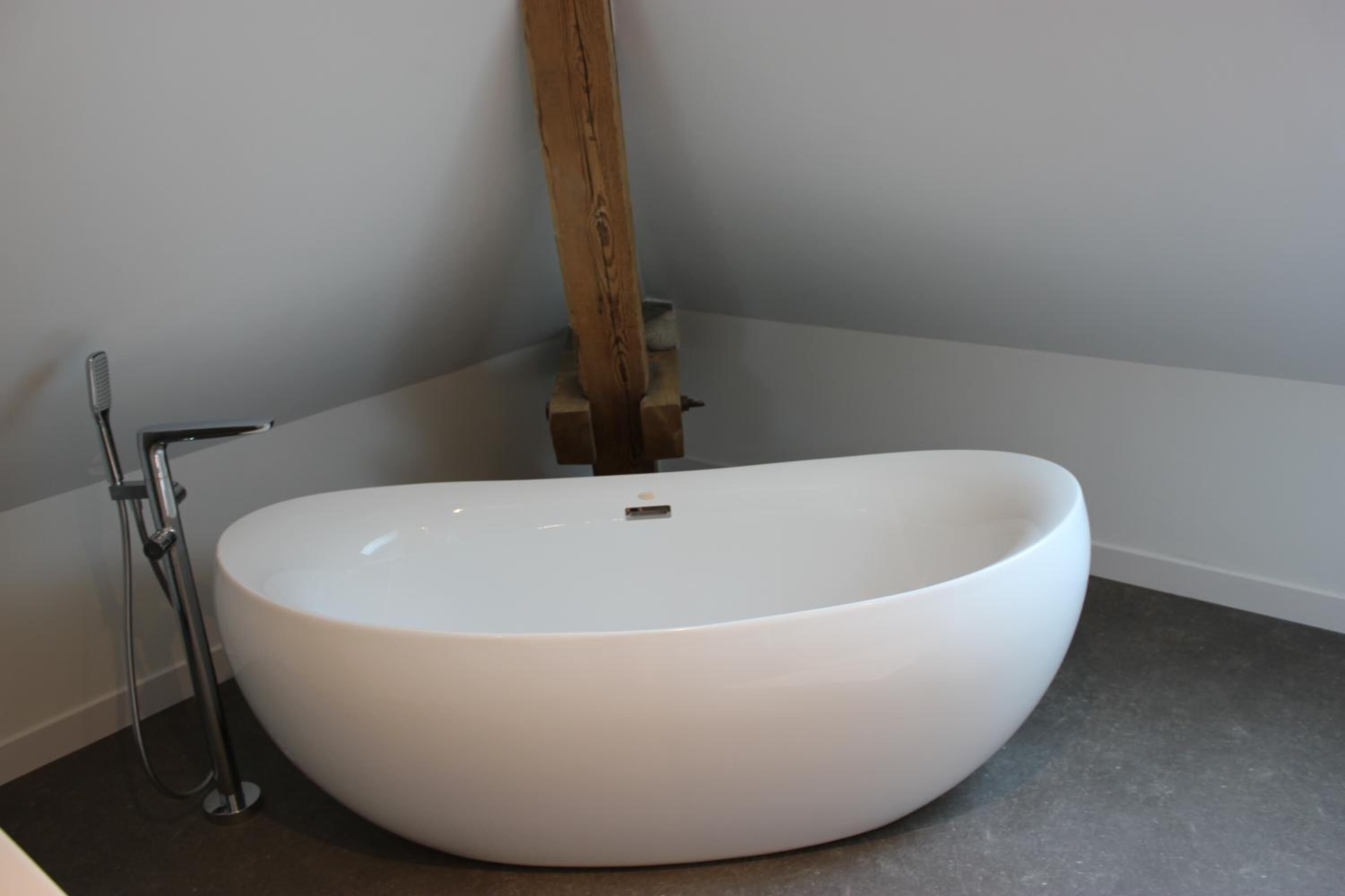 Un baño moderno con un lavamanos ovalado grande, un cabezal de ducha de mano y una pared decorativa de madera.