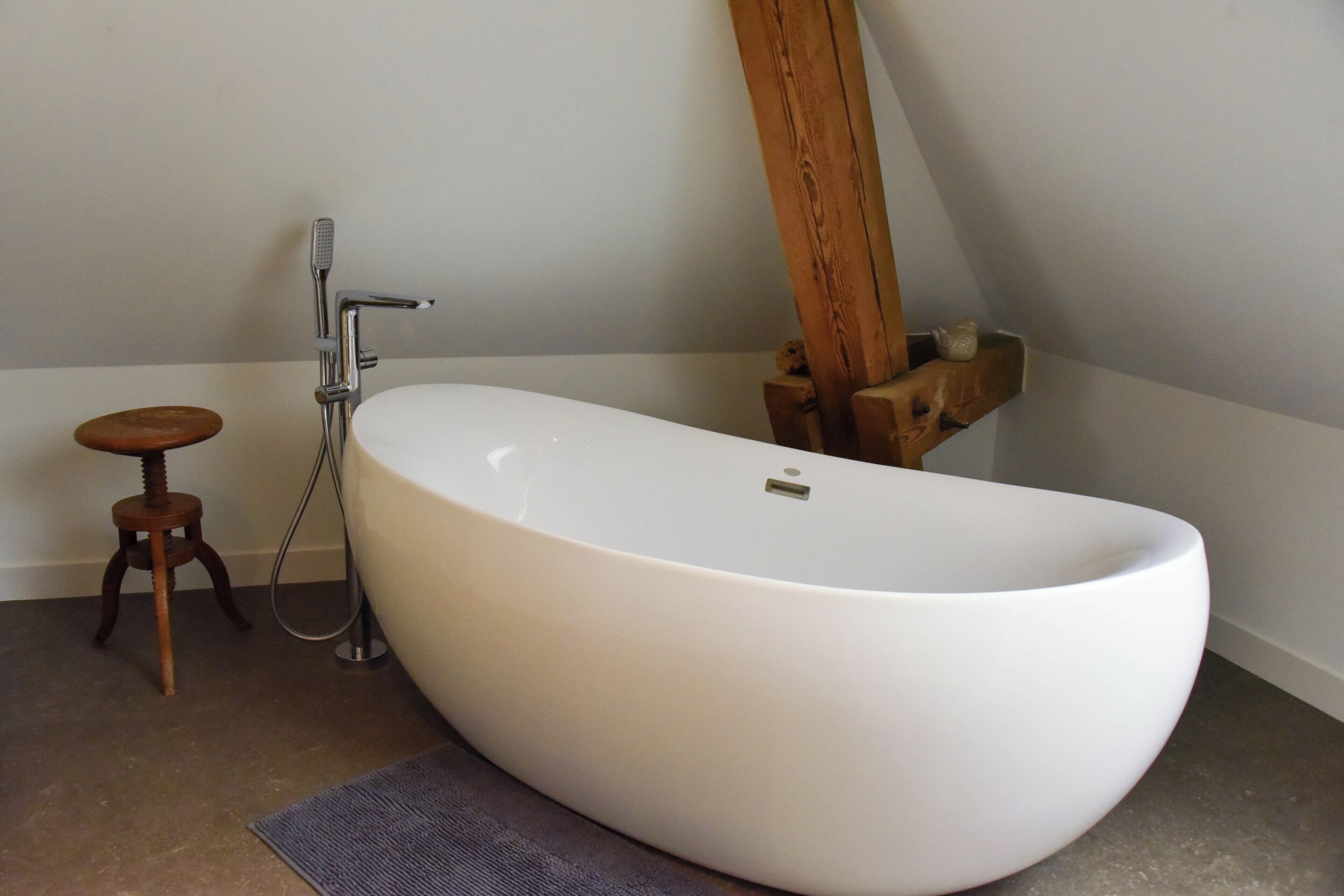 A modern bathroom with a freestanding bathtub, a wooden stool, and a wooden shelf.