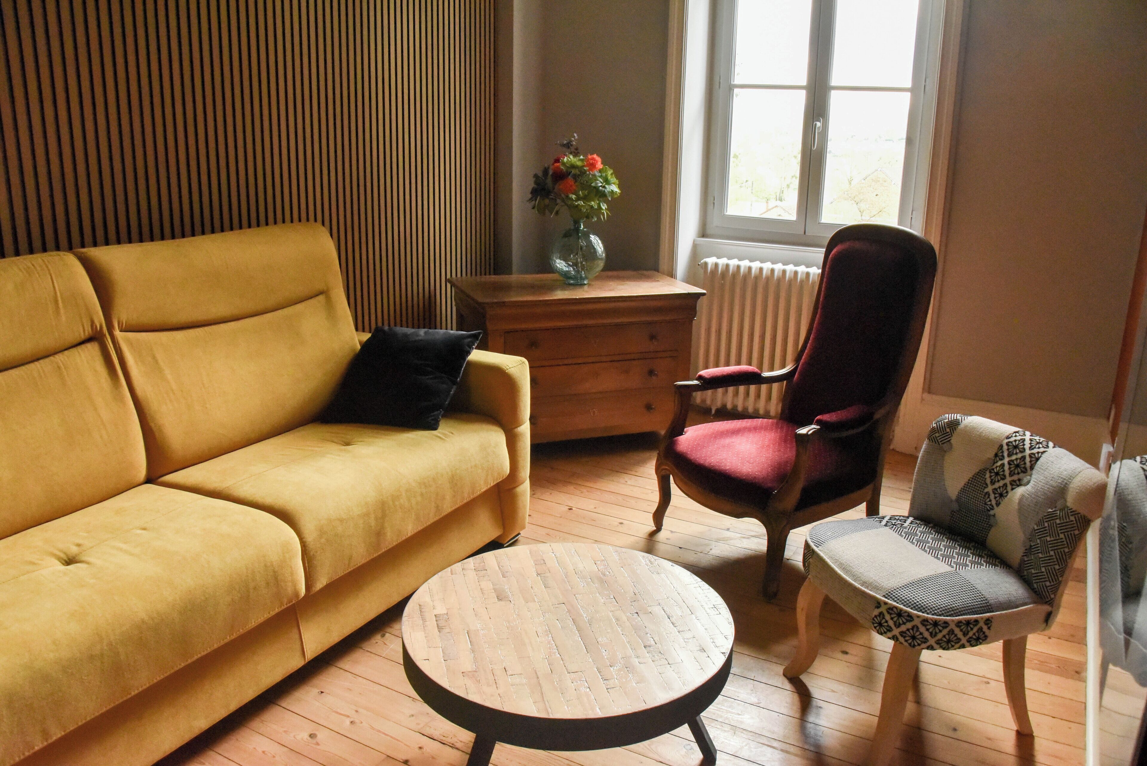 A living room with a yellow sofa, a wooden coffee table, a red chair, and a patterned armchair.
