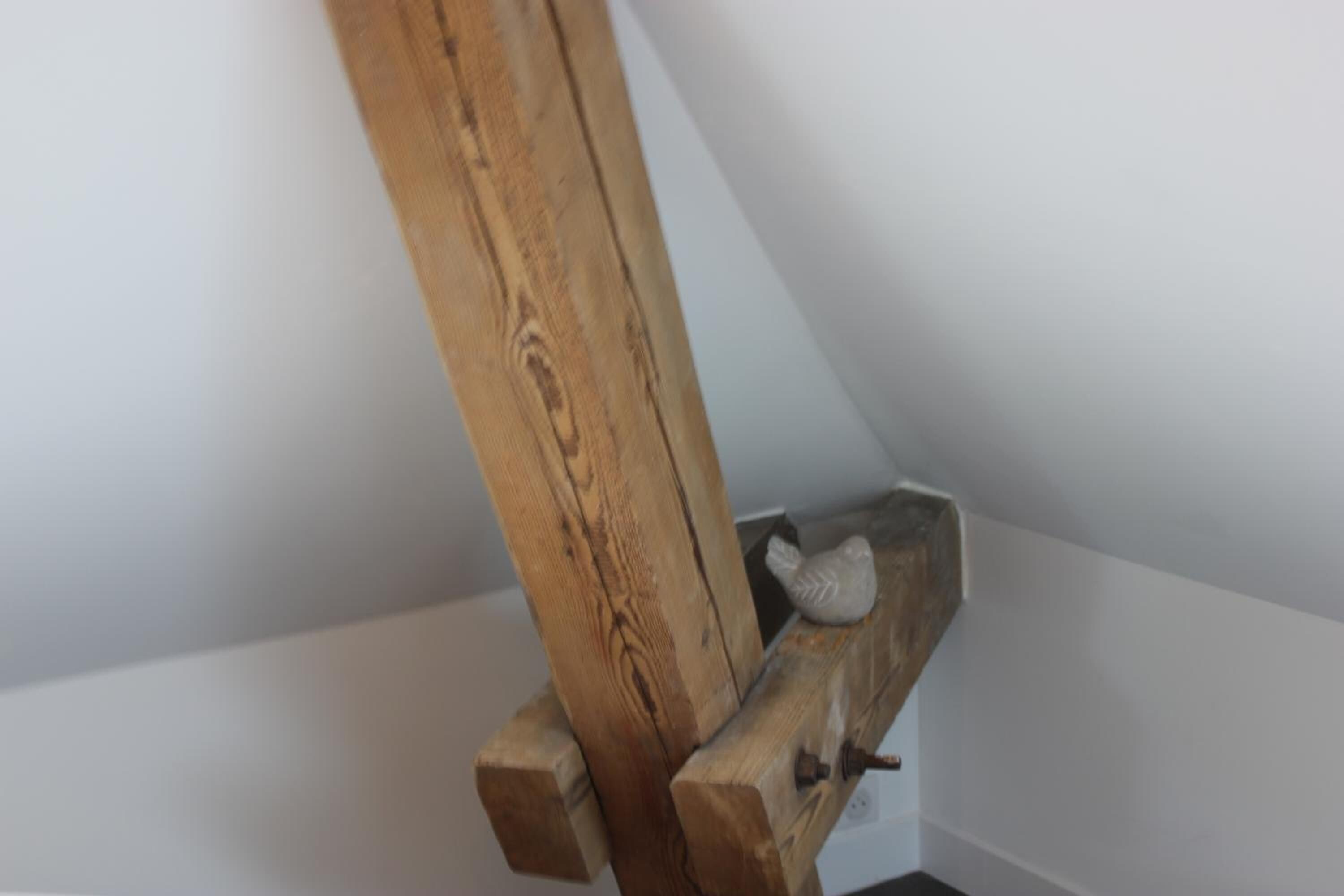Rincón de una habitación con una viga de madera y un pequeño estante con un objeto decorativo.