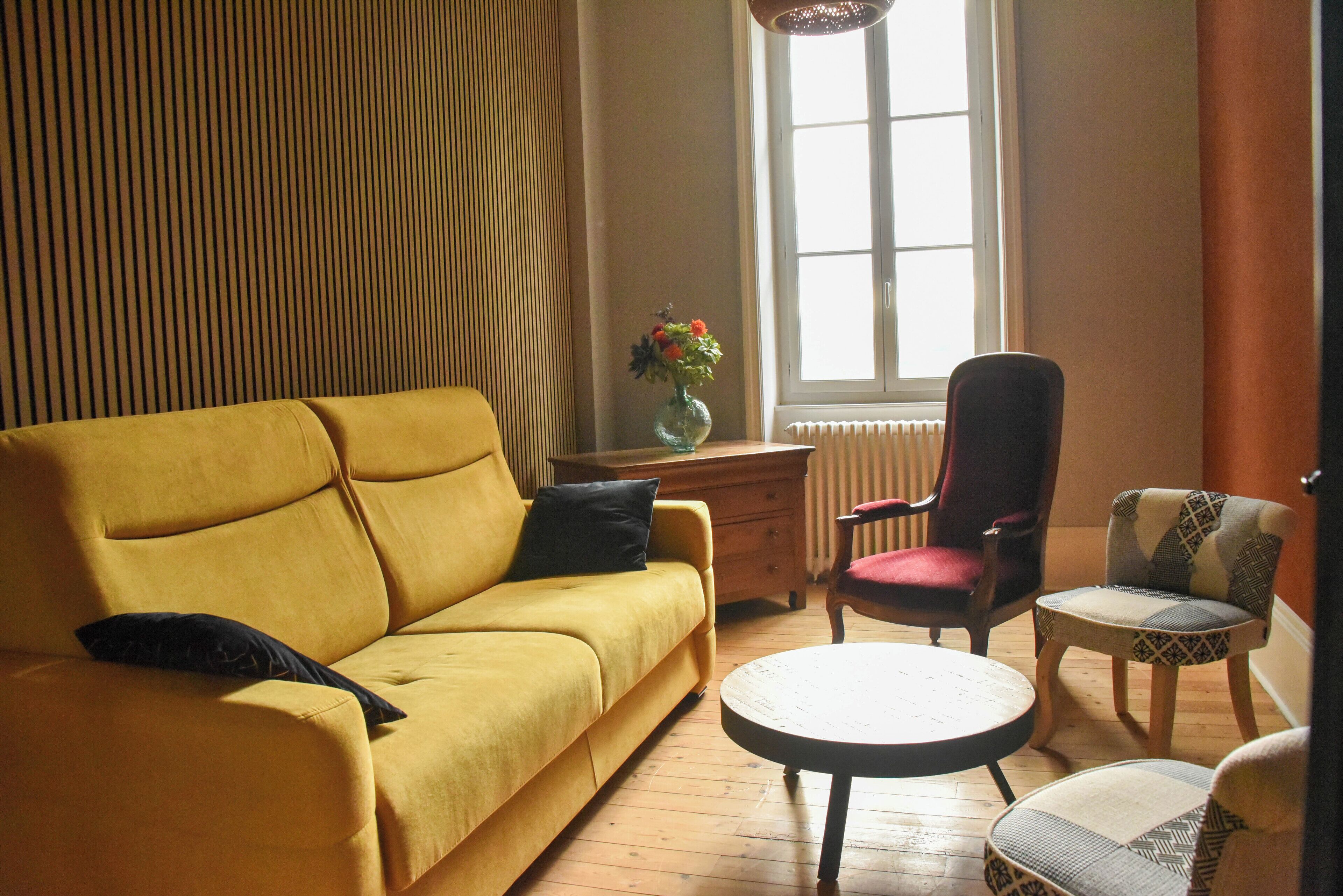 Een woonkamer met een geel sofa, een ronde salontafel, een rode fauteuil en een gestreept fauteuil.