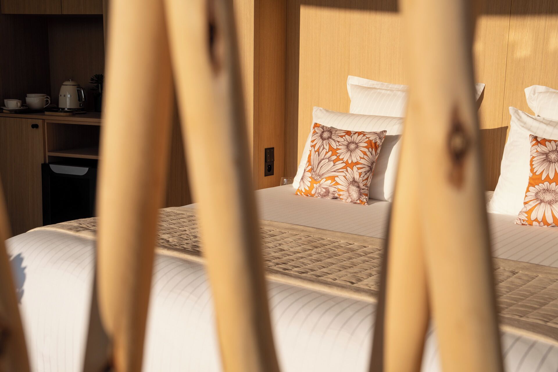 A neatly made bed with floral pillows, a wooden headboard, and a bedside table with a kettle and cups.