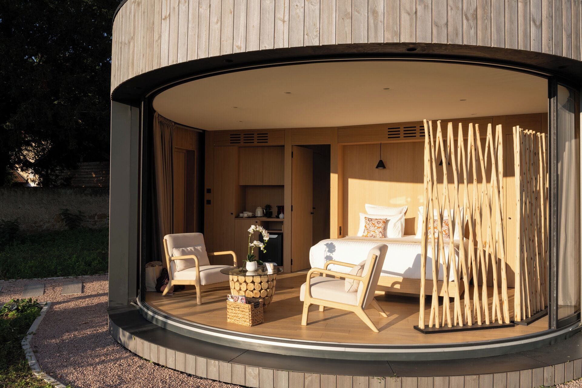 A modern, circular room with a bed, two chairs, and a small table.