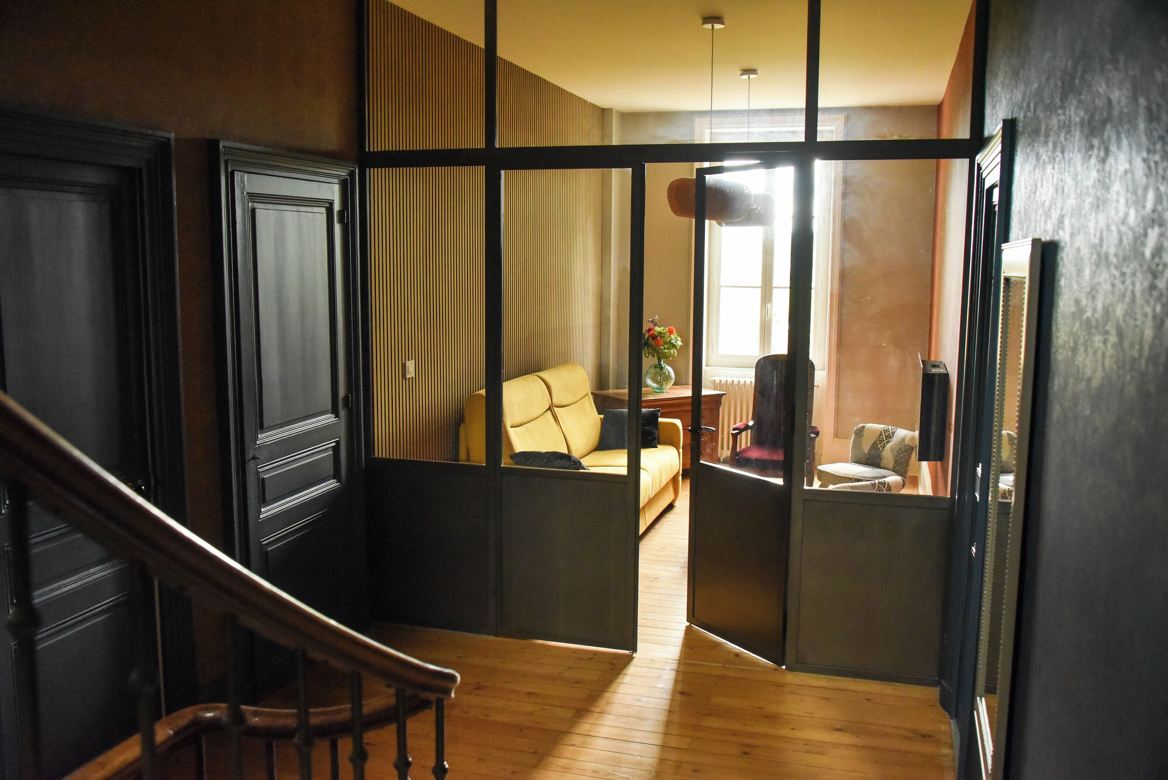 A hallway with a wooden staircase, a sofa, and a chair in a room with a large window.