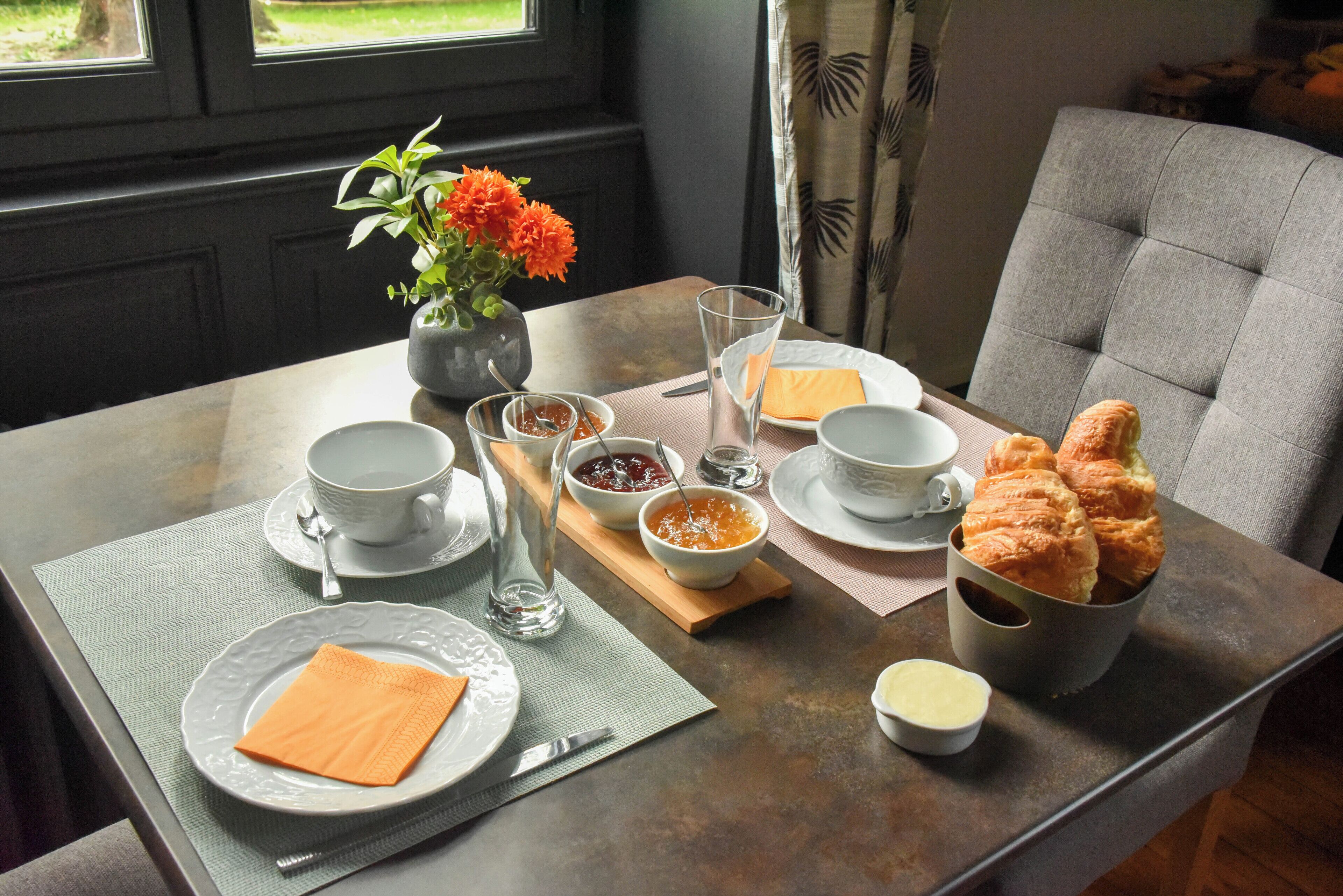 A dining table set with plates, cups, a vase of flowers, and a basket of pastries.