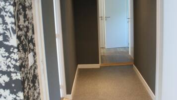 A narrow hallway with carpeted flooring, a door at the end, and patterned wallpaper on one side.