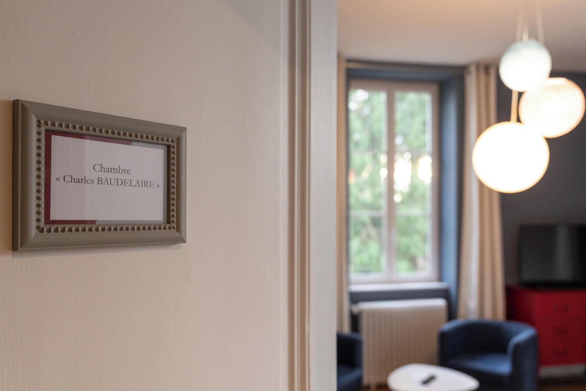 A framed nameplate on a wall, a window with a view of greenery, and a modern light fixture.