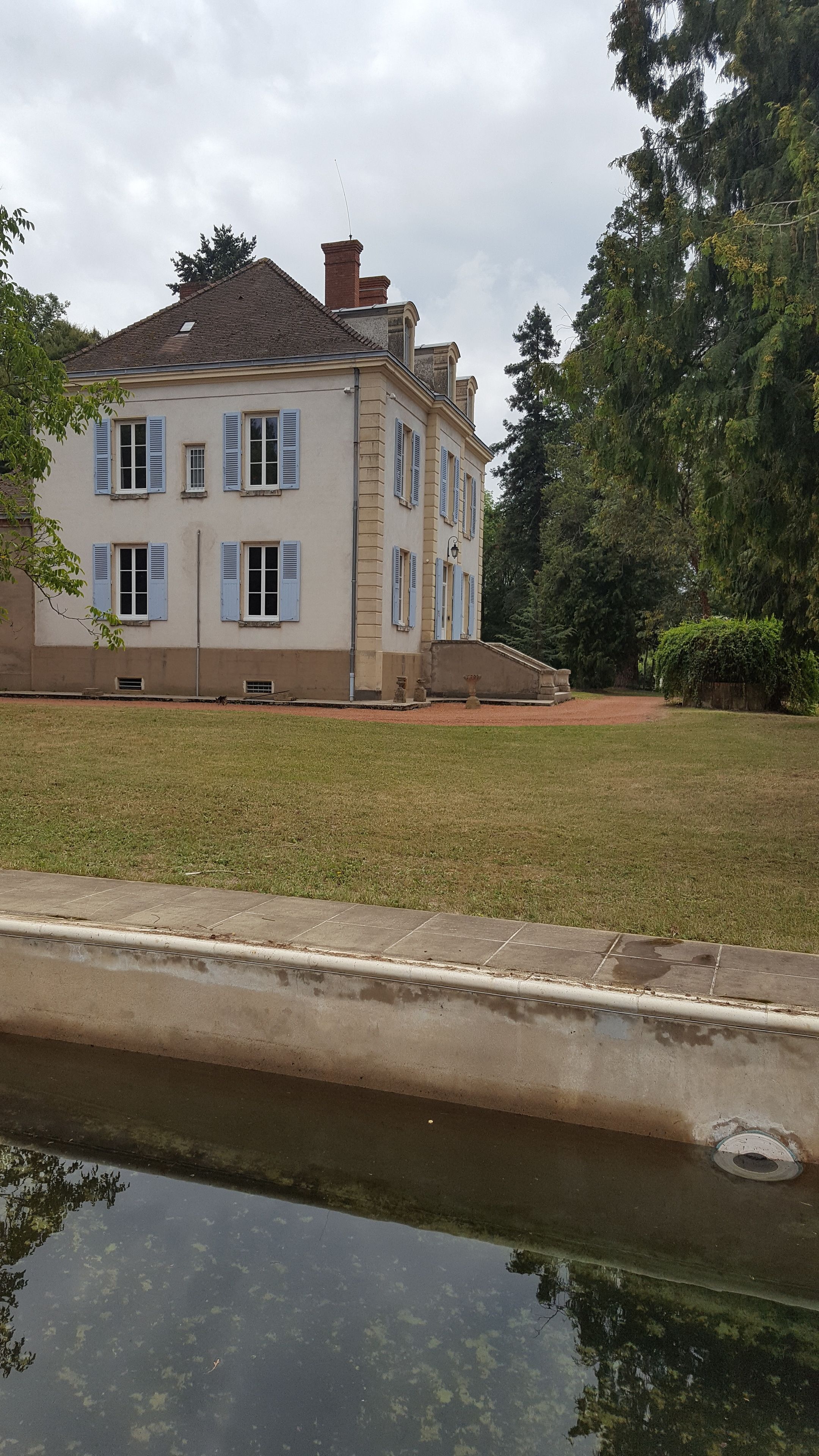 Un grand bâtiment à deux étages, doté d’une façade symétrique, d’une entrée centrale et d’un petit jardin à l’avant.