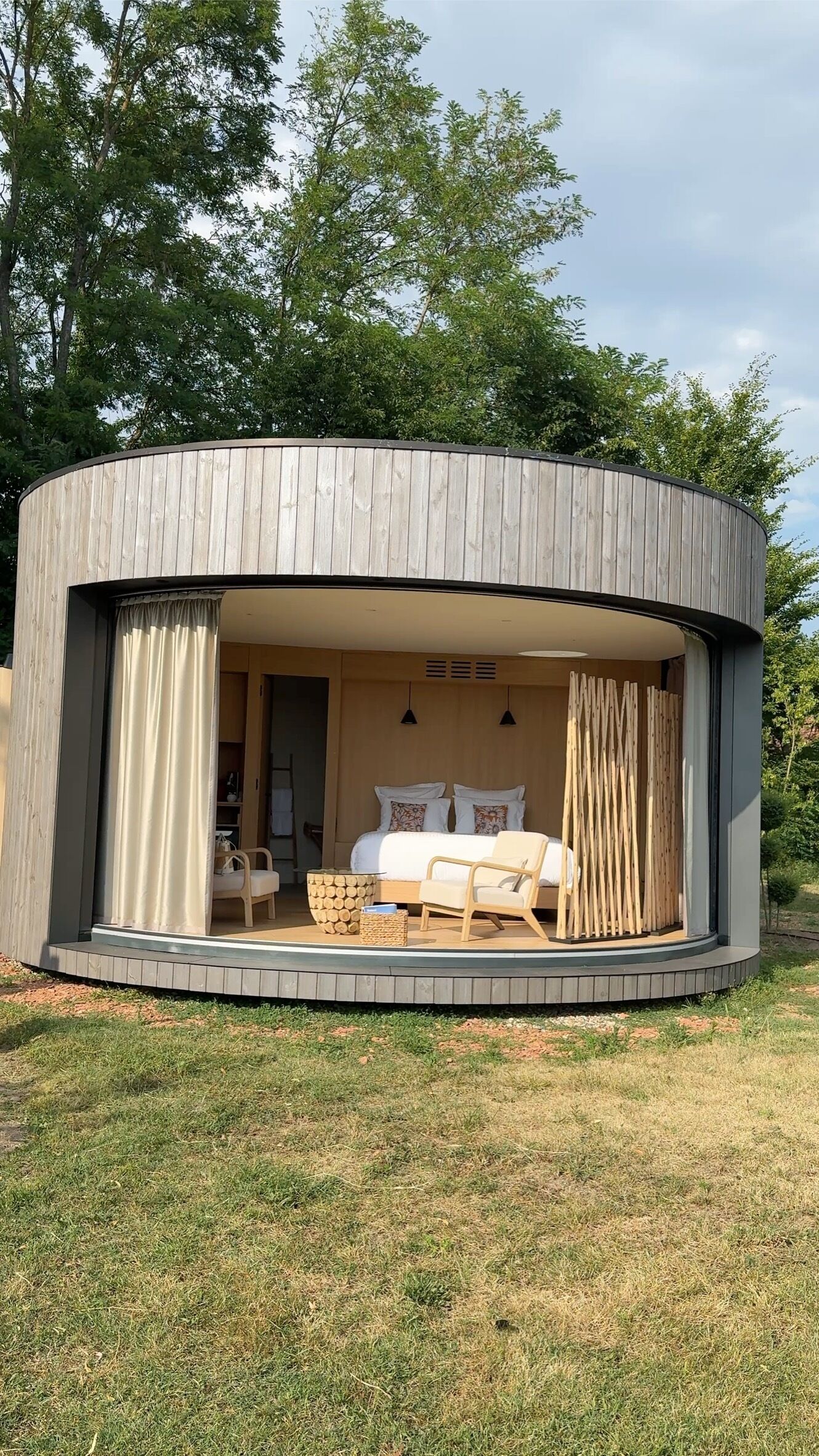 Una estructura circular de madera con una cama, cortinas y un pequeño rincón de descanso.