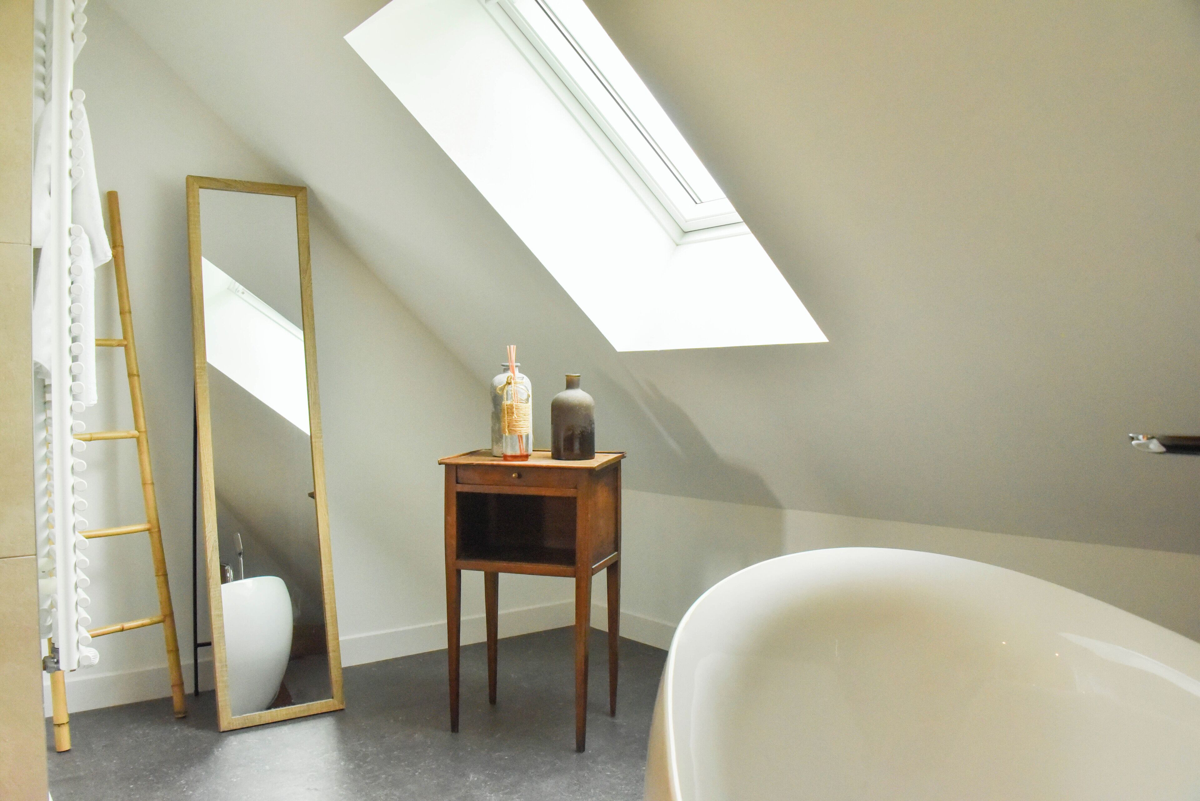 A bathroom with a skylight, a wooden ladder, a mirror, a small table with candles, and a bathtub.