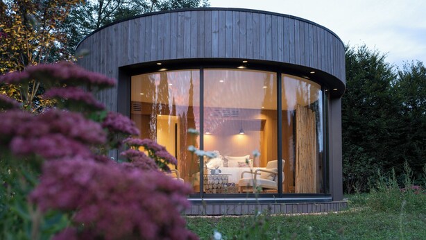 A modern, circular wooden cabin with large windows, a sofa, and a table inside. - Clos Marie (Iguerande)
