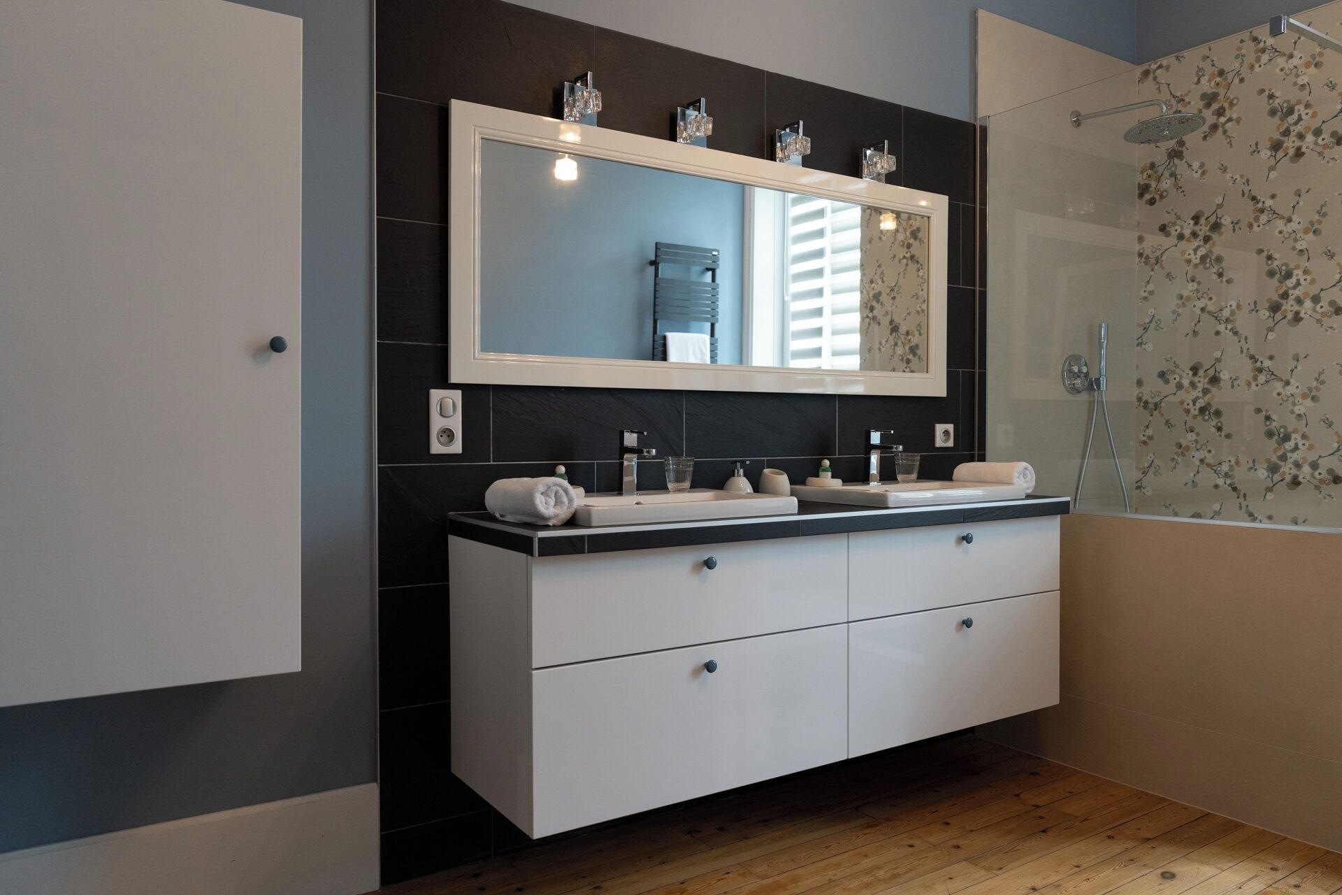 Une salle de bain moderne avec un grand miroir, deux lavabos, une douche et un plancher en bois.