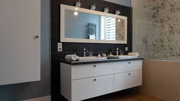 Une salle de bain moderne avec un grand miroir, deux lavabos, une douche et un plancher en bois.