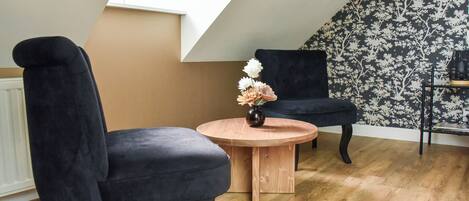 A room with two black chairs, a wooden table with a vase of flowers, and a patterned wallpaper.