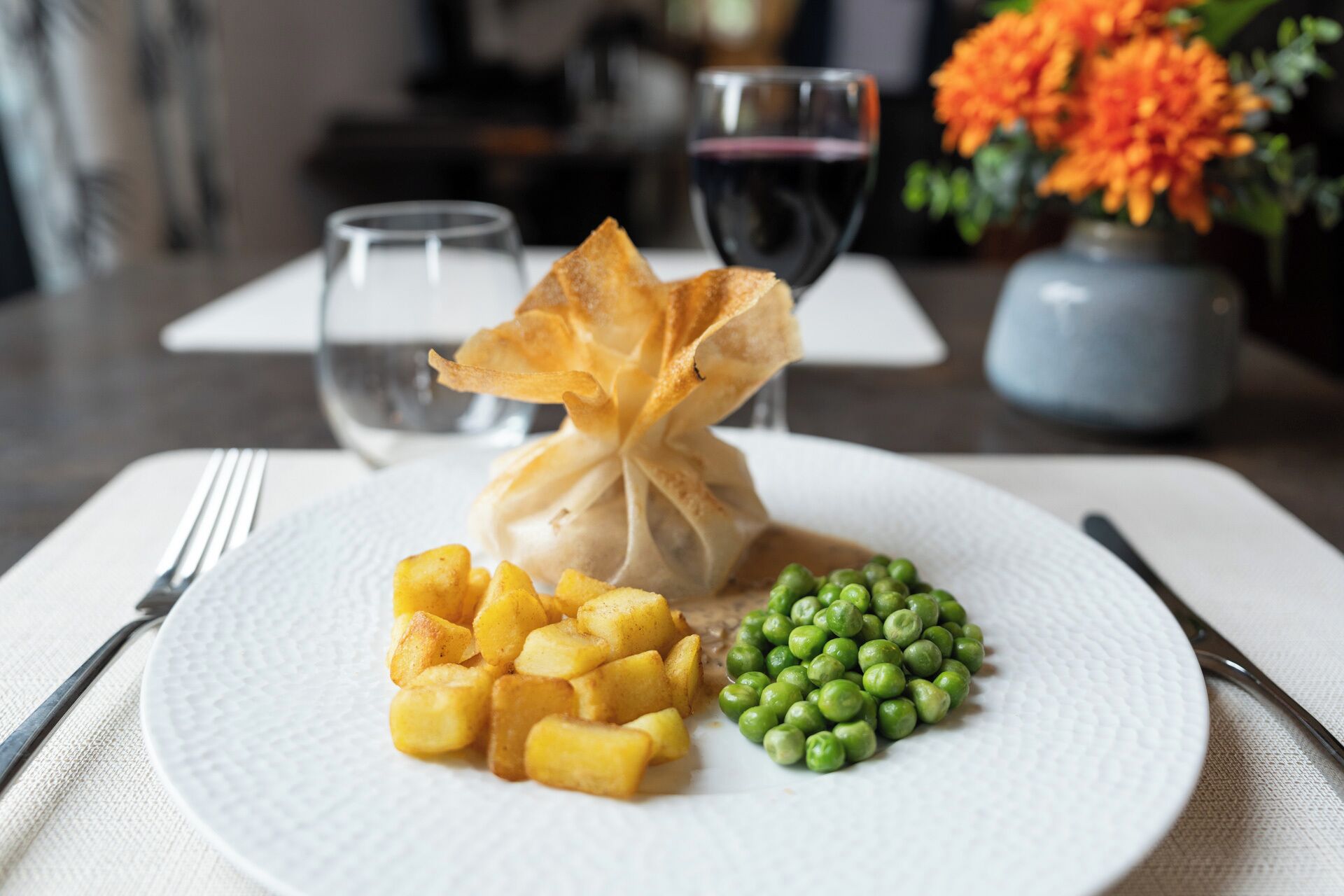 A plate with a dumpling, diced potatoes, and peas, accompanied by a fork and knife on a napkin.