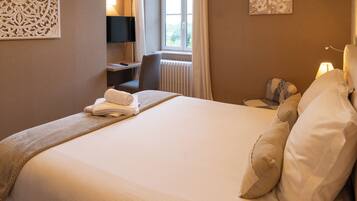 Een netjes opgemaakt bed met een opgerolde witte handdoek, een nachtkastje met een lamp en een stoel.