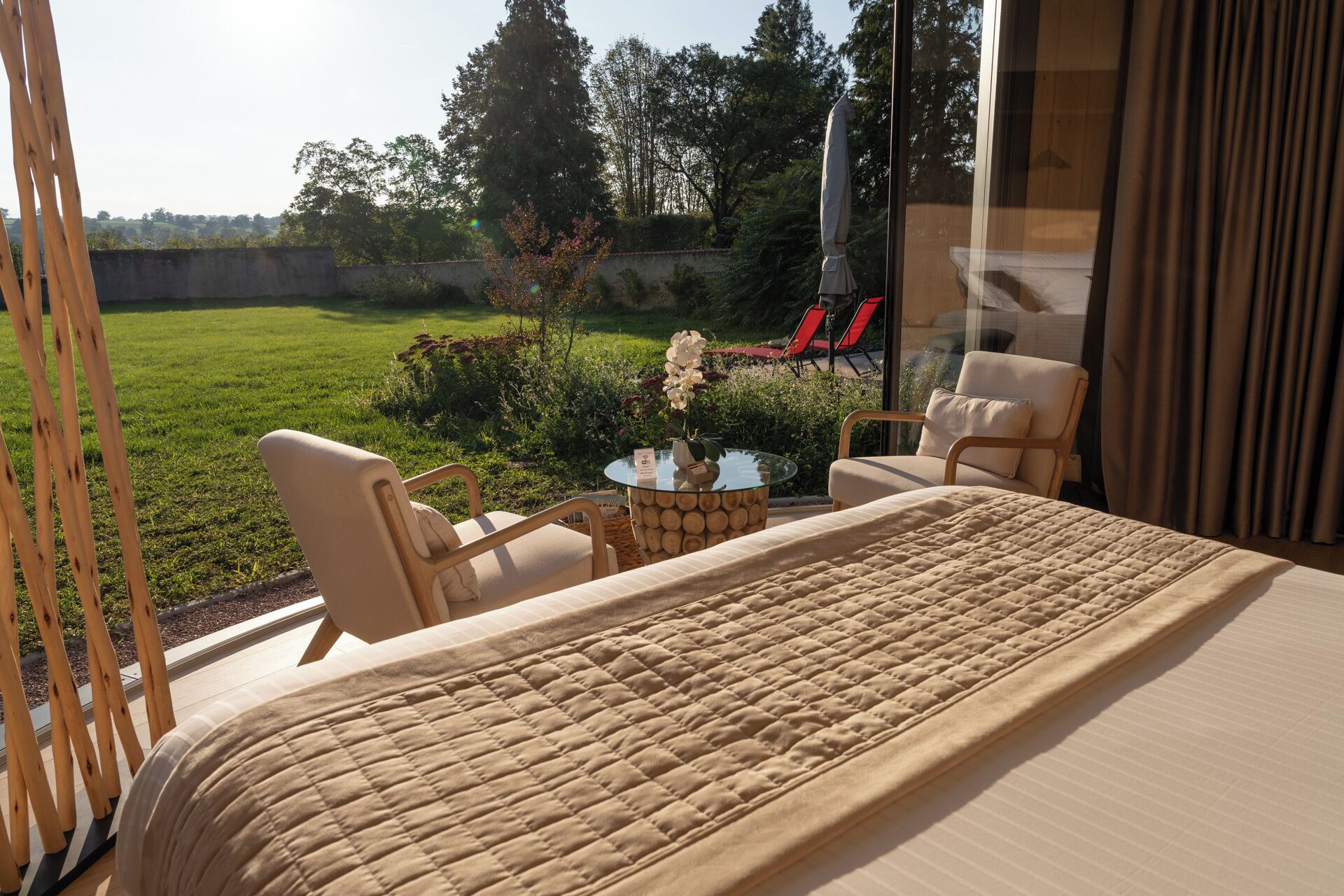 A bedroom with a large bed, two chairs, a small table, and a view of a garden.