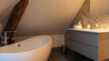 A modern bathroom with a freestanding bathtub, a vanity with a mirror, and patterned tiles on the walls.
