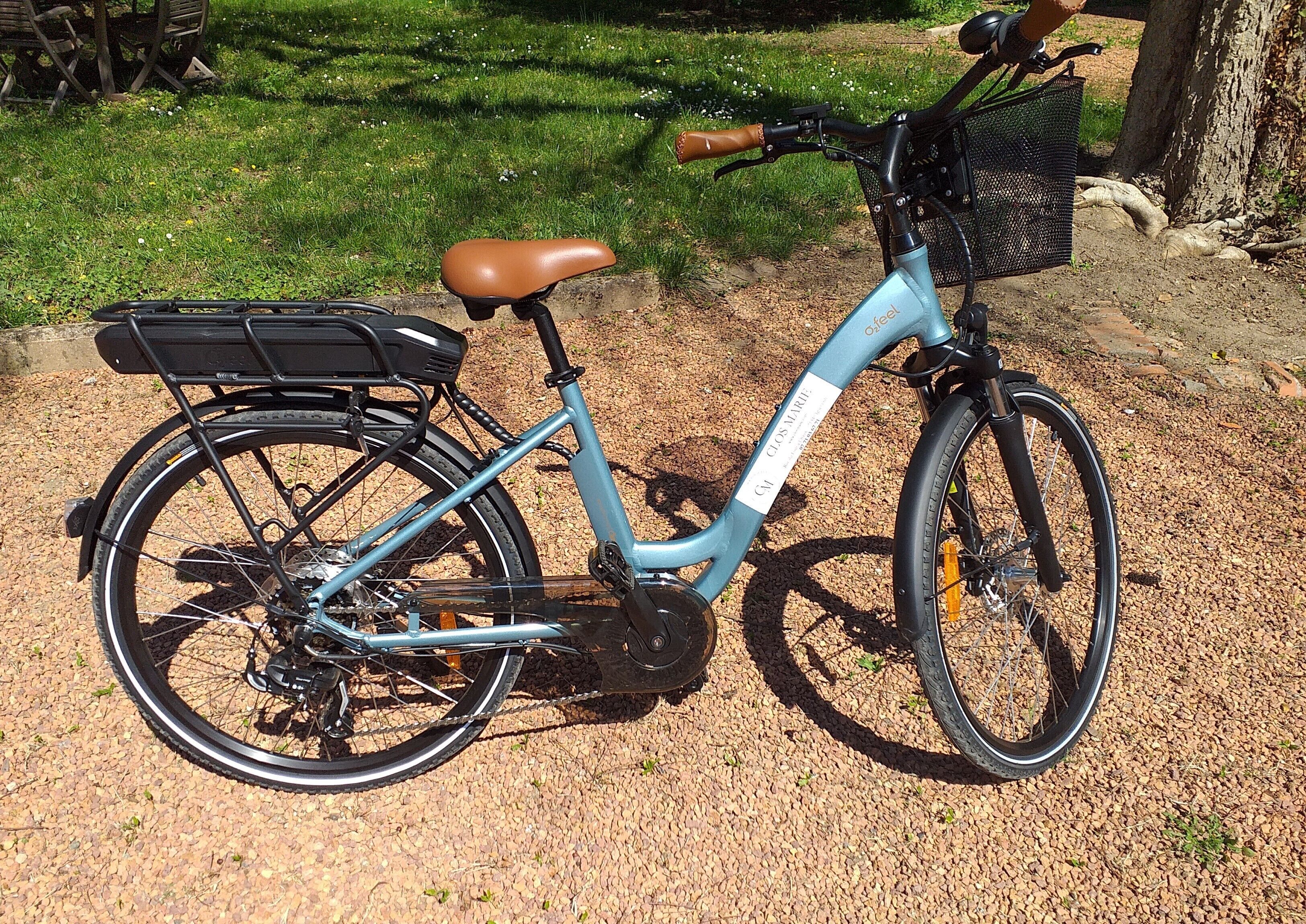 Una bicicleta eléctrica estacionada sobre grava, con asiento marrón y canasta trasera.