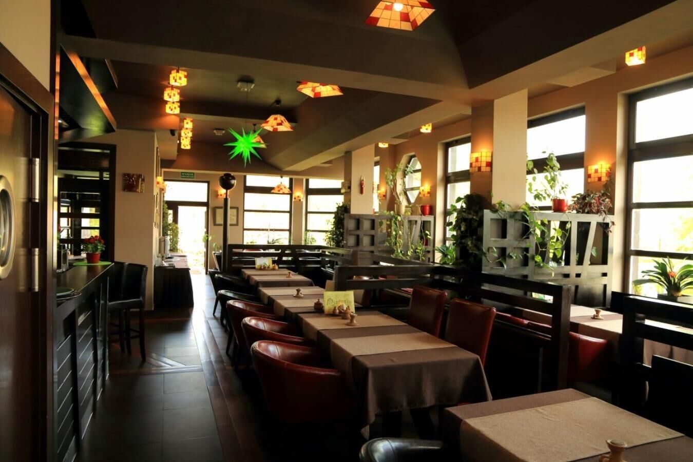 A restaurant with long tables and booths, large windows, and hanging light fixtures.