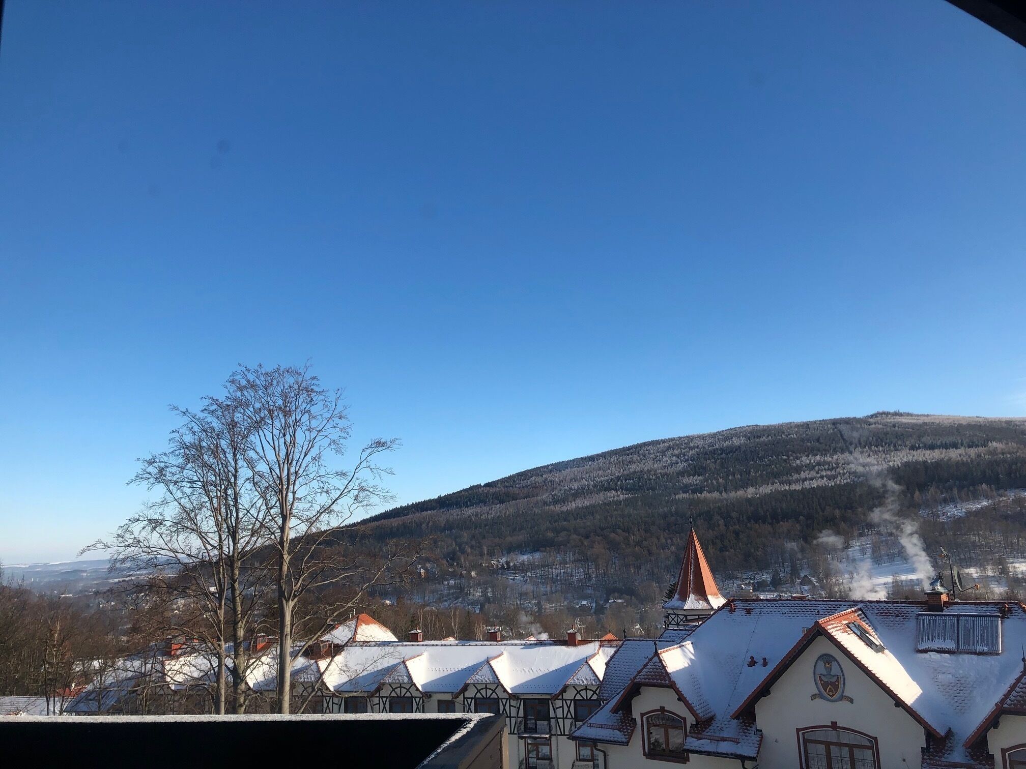 A town with traditional buildings, a church with a red roof, and a snow-covered hill in the background.
