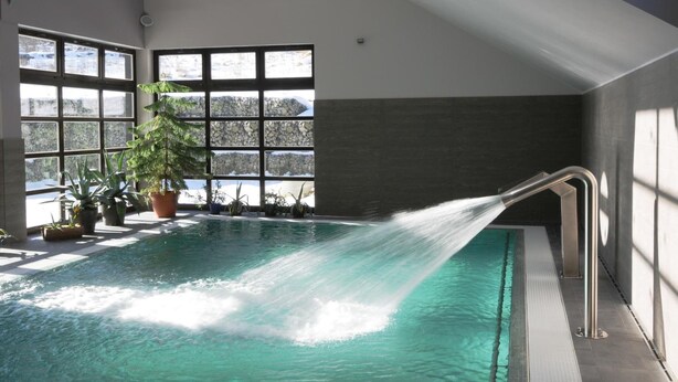 Una piscina interior con tobogán de agua, ventanas amplias y plantas en macetas.