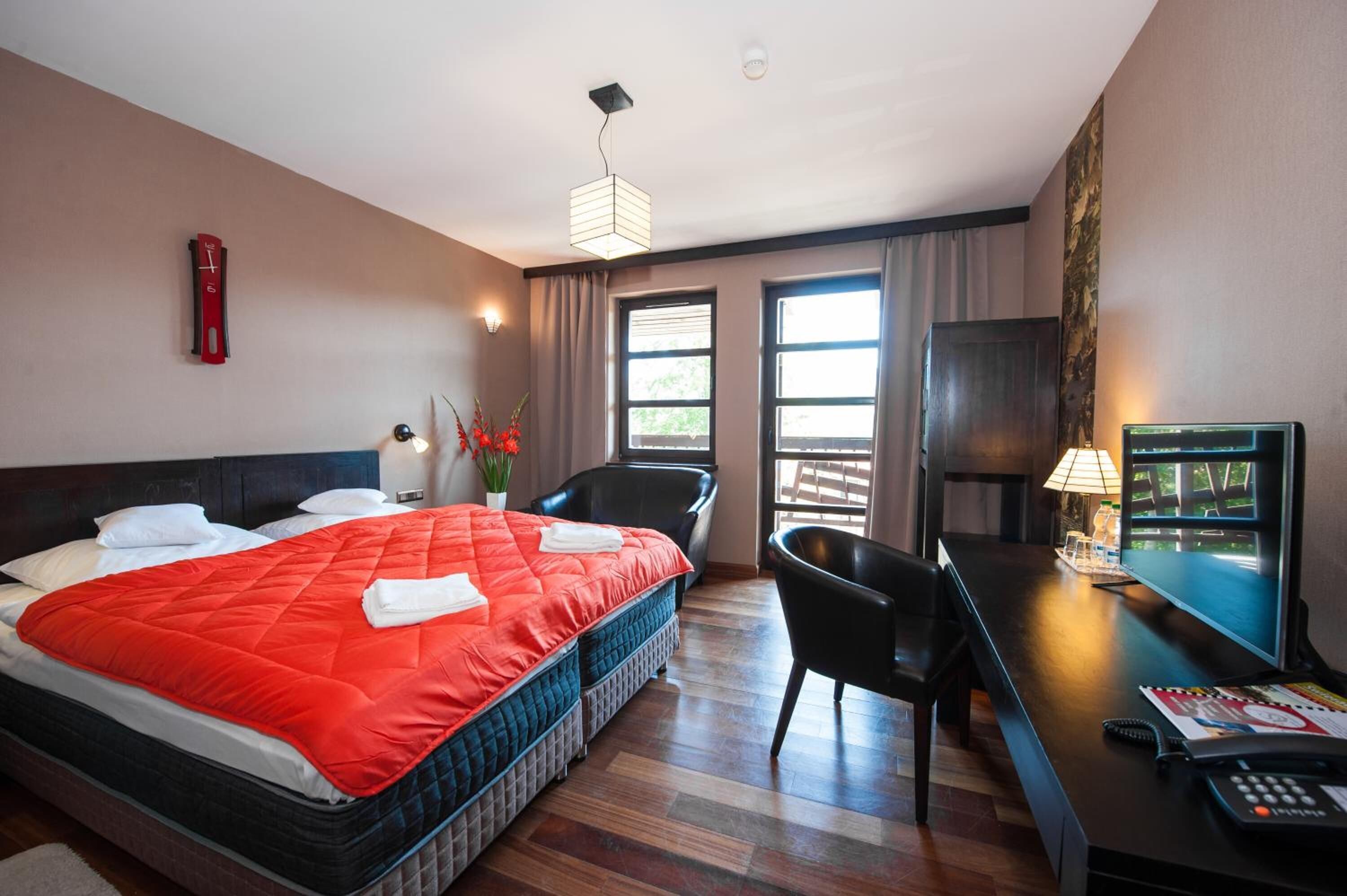 A hotel room with a large bed, a desk with a computer, a chair, and a window with curtains.