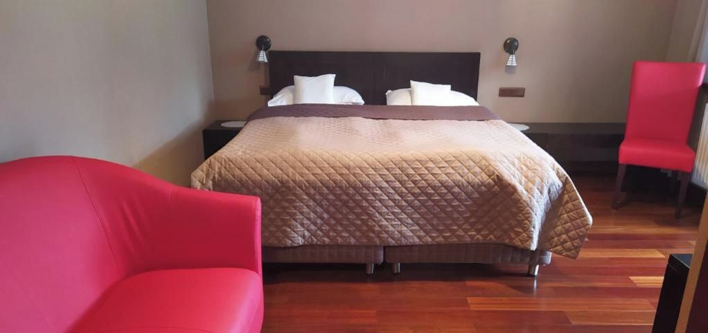 A hotel room with a bed, two bedside tables, a red chair, and a red armchair.